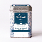 A metal tin of Maison Gabrielle mustard seeds, featuring a blue and white floral pattern with a dark blue label, set against a plain white background.